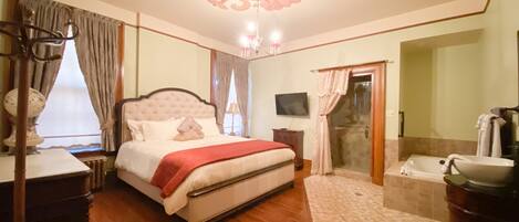 A bedroom with a large bed, a vanity with a sink, and a shower area.