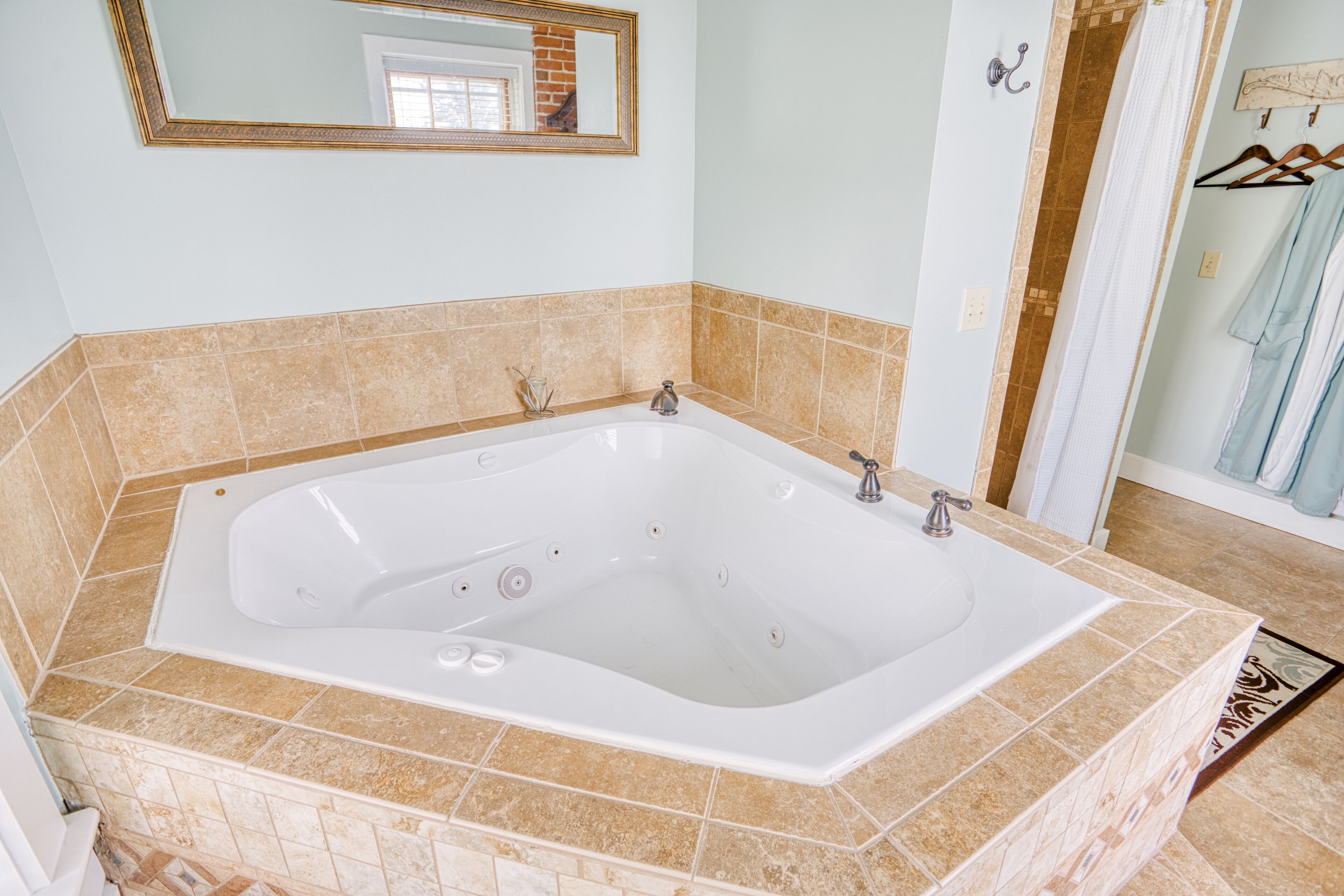 Un baño con una bañera grande, azulejos color beige, un espejo y un perchero para toallas.
