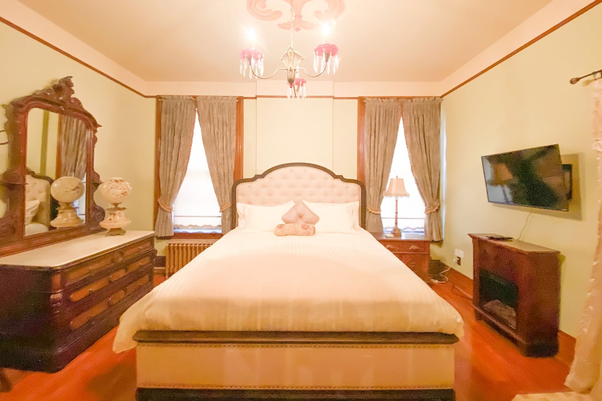 Ein Schlafzimmer mit einem großen Bett, einem Schminktisch, einem Spiegel, einer Chandelier und einem Fernseher.