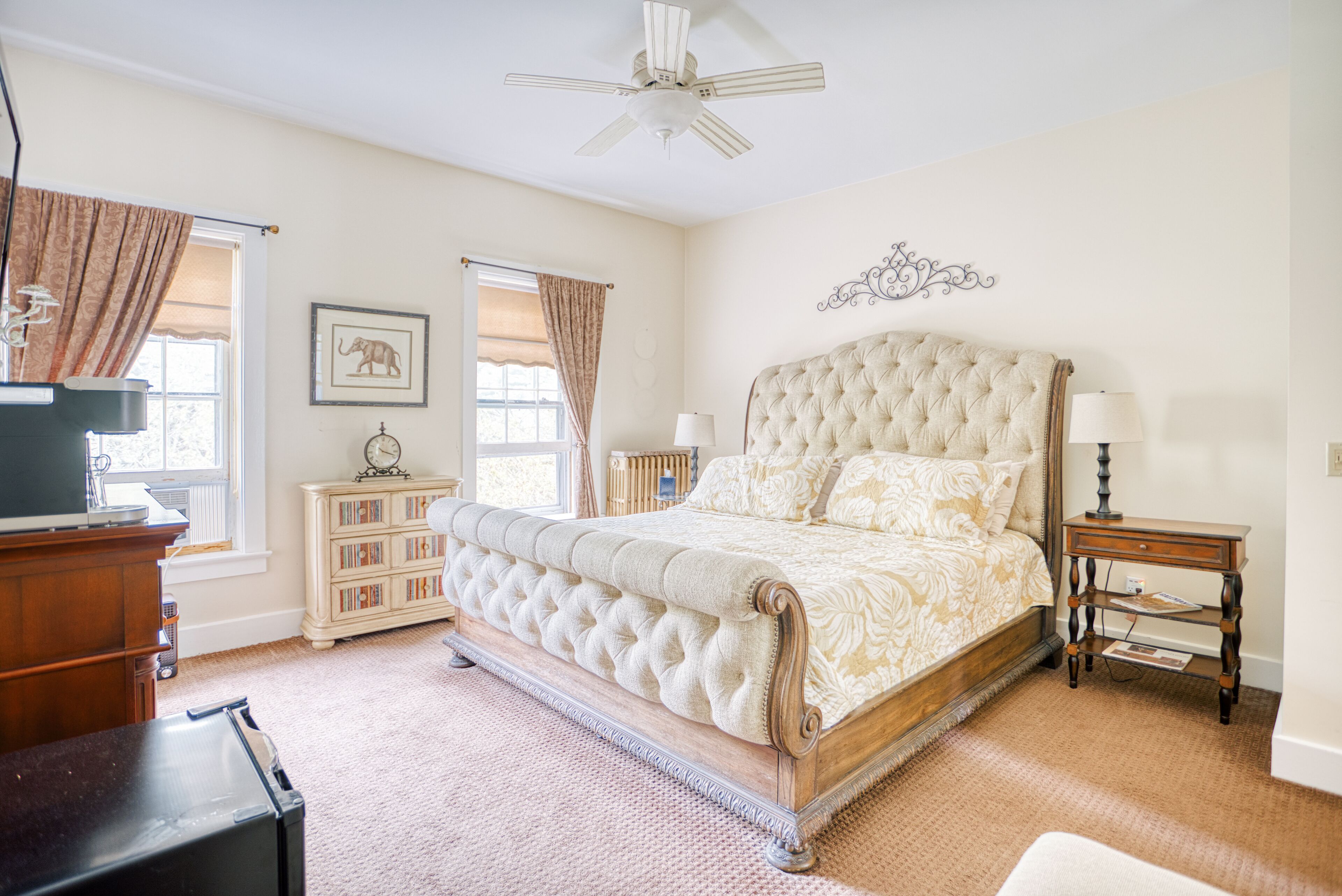 A bedroom with a large bed, a ceiling fan, a dresser, a nightstand, and a bookshelf.
