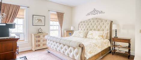 A bedroom with a large bed, a ceiling fan, a dresser, a nightstand, and a bookshelf.