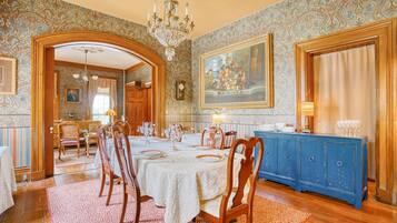 A dining room with a long table set for six, surrounded by wooden chairs. A blue cabinet with glassware is against the wall.