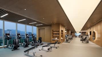 A modern gym with cardio machines, weightlifting equipment, and large windows offering city views.