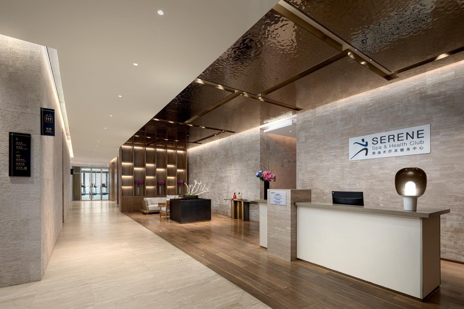 A modern spa and health club interior with a reception desk, seating area, and directional signs.