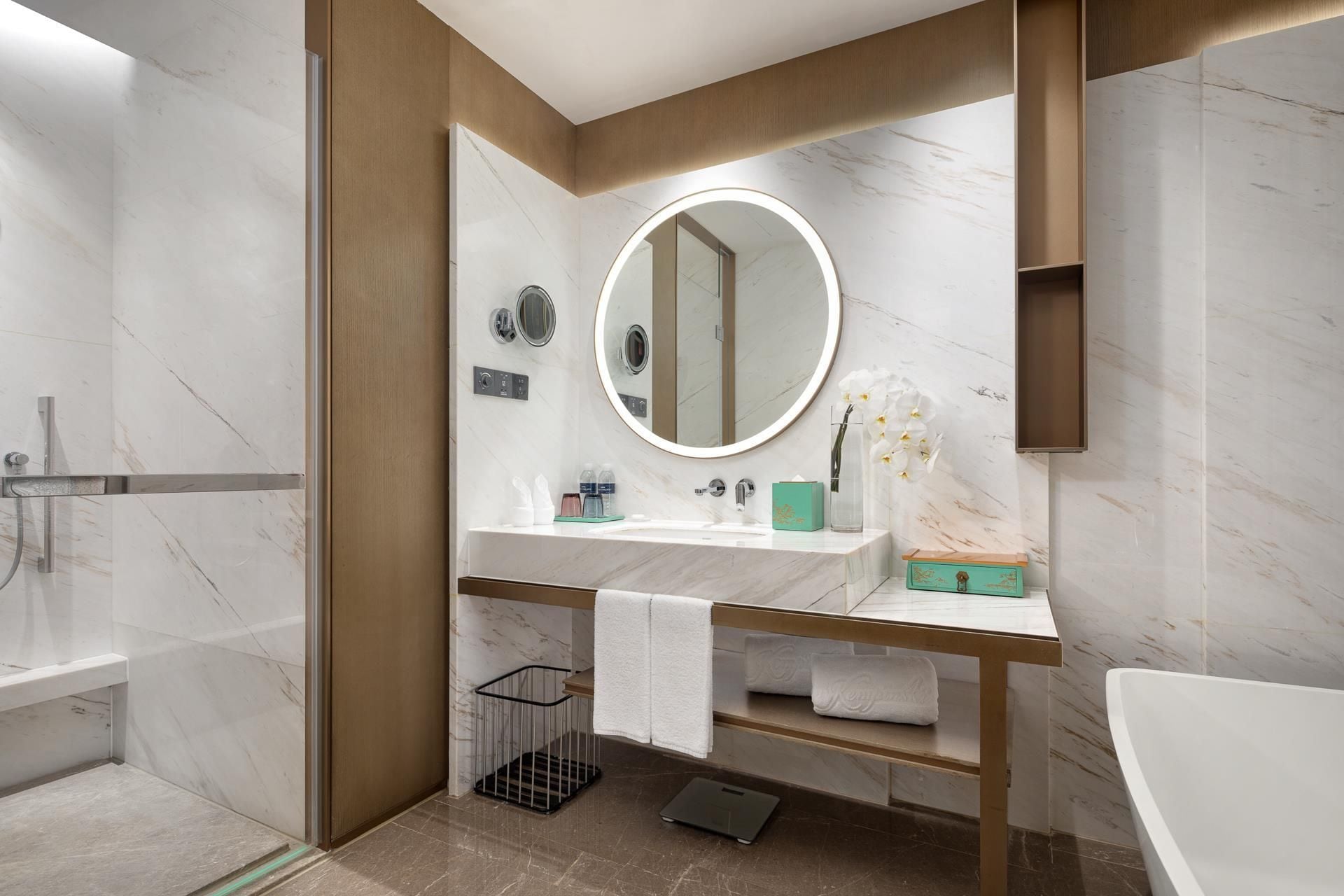 A modern bathroom with a marble vanity, a round mirror, a bathtub, and a shower area.