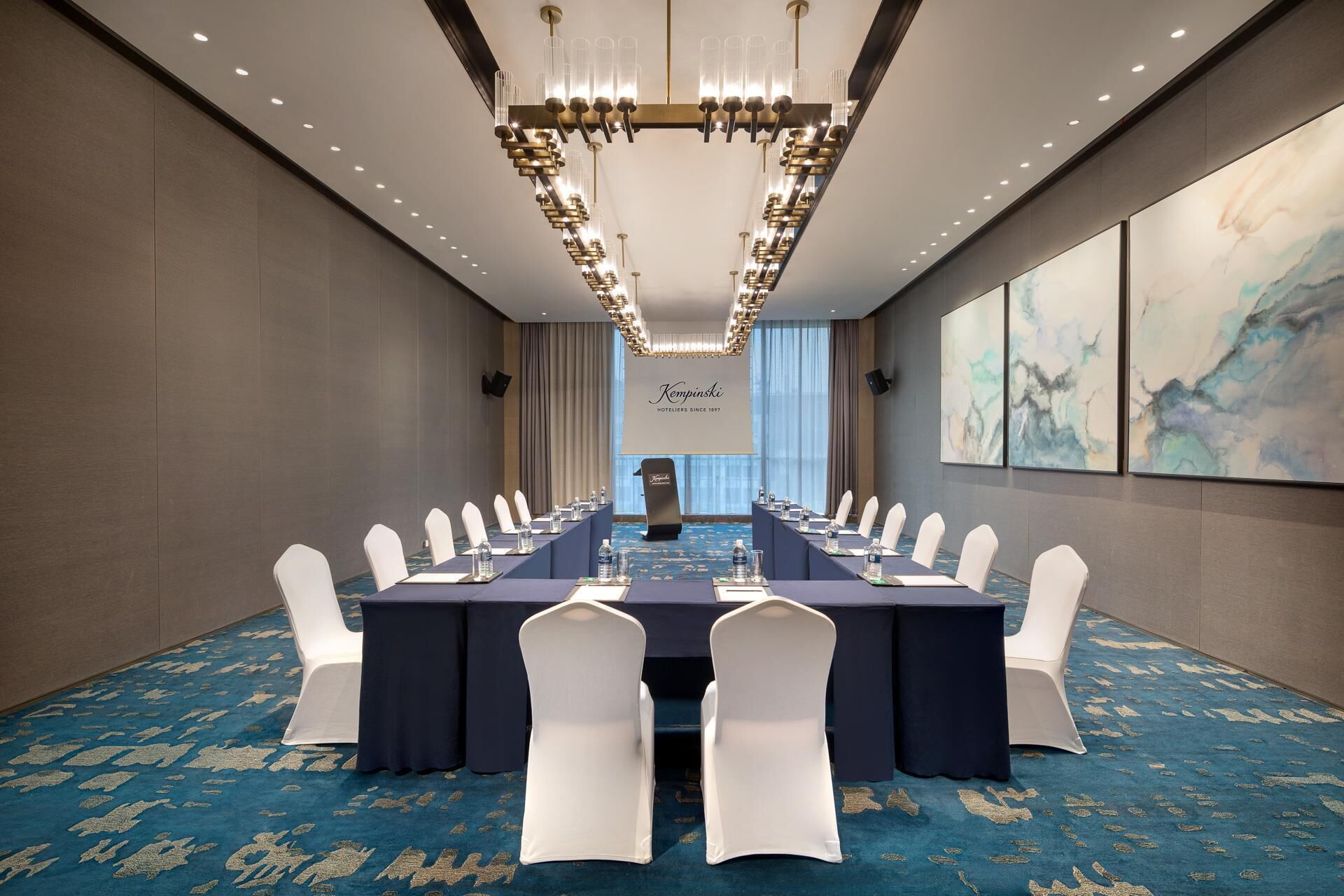 A conference room with a long table, white chairs, and a chandelier.