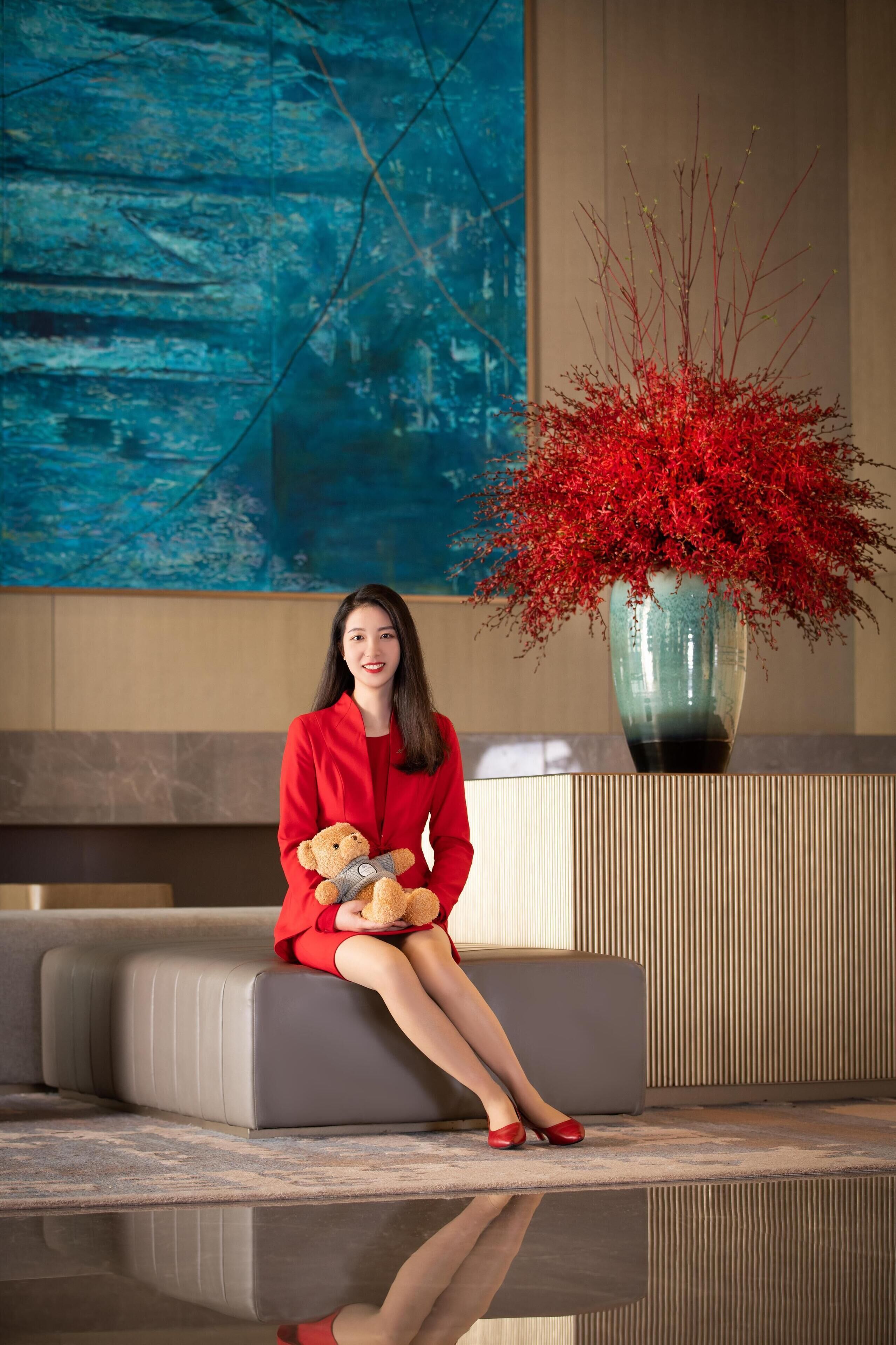 Eine Person sitzt auf einem grauen Sofa in einer Lobby mit einer großen, roten floralen Dekoration und einem blauen, abstrakten Gemälde an der Wand.