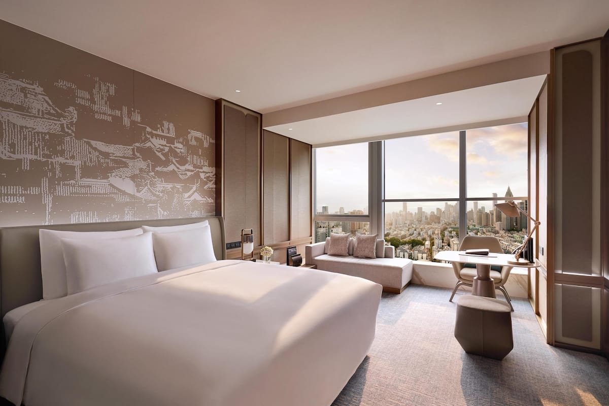 Une chambre d’hôtel moderne dotée d’un grand lit, d’un coin salon et offrant une vue sur la ville grâce à de grandes fenêtres.