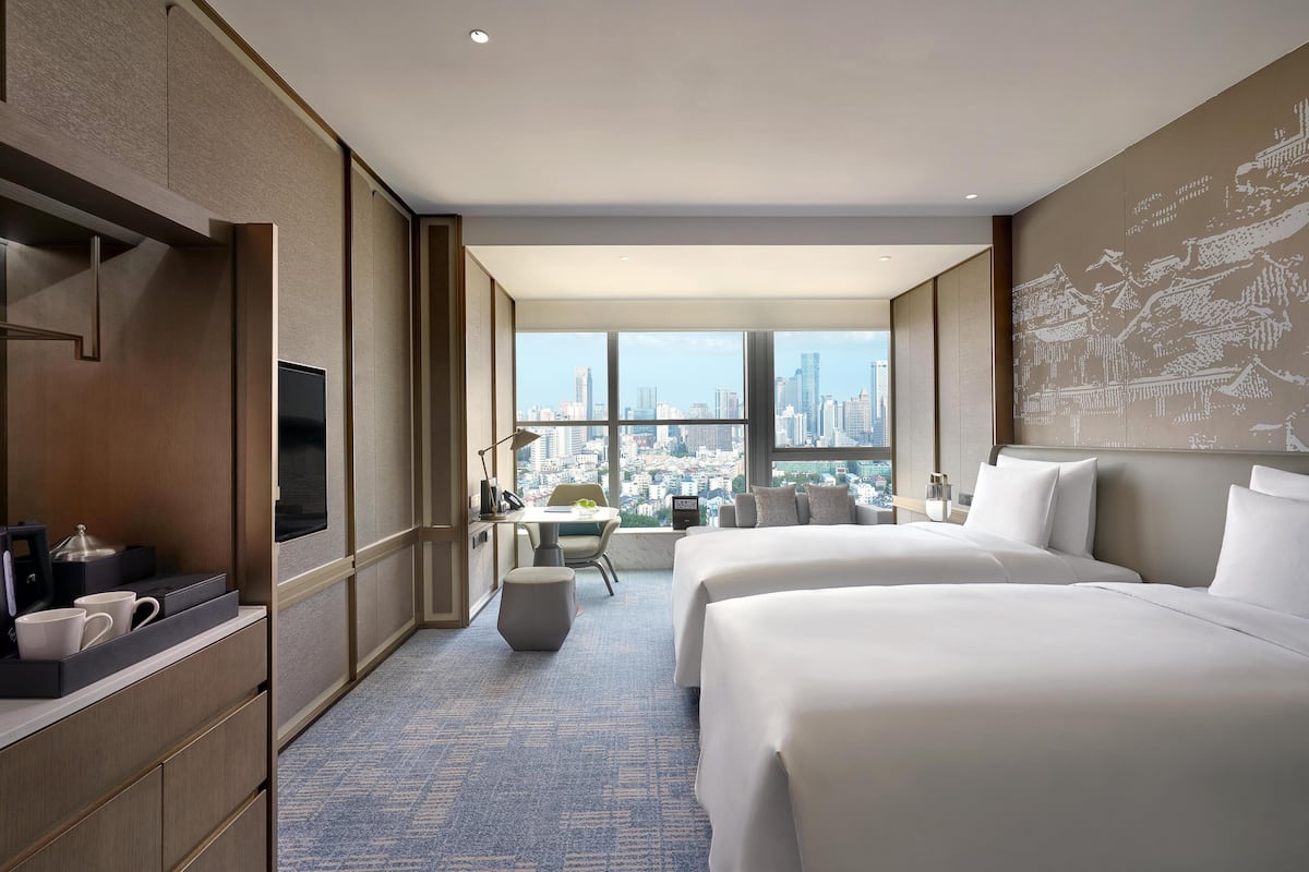 Une chambre d’hôtel avec deux lits, un bureau, une télévision et une grande fenêtre donnant sur la ville.