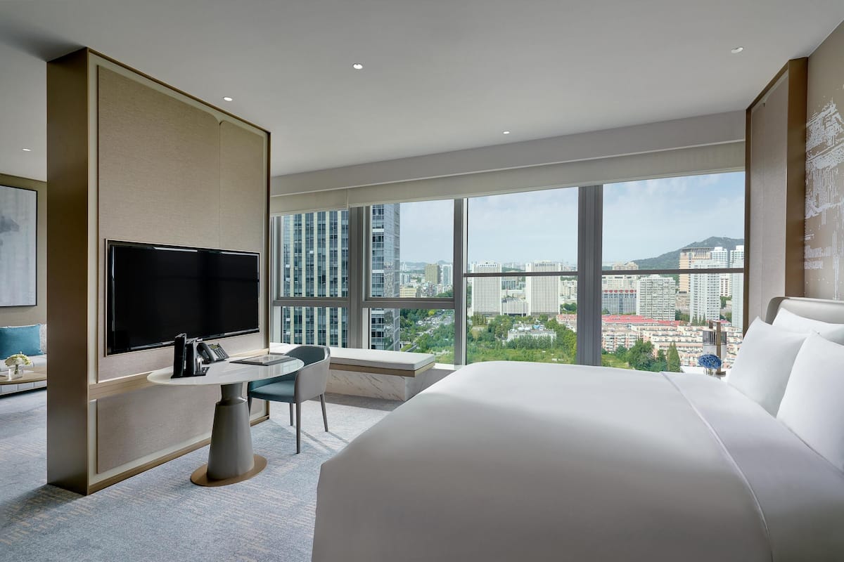Une chambre d’hôtel moderne dotée d’un grand lit, d’un téléviseur à écran plat, d’une petite table à manger et offrant une vue sur le paysage urbain grâce à de grandes fenêtres.