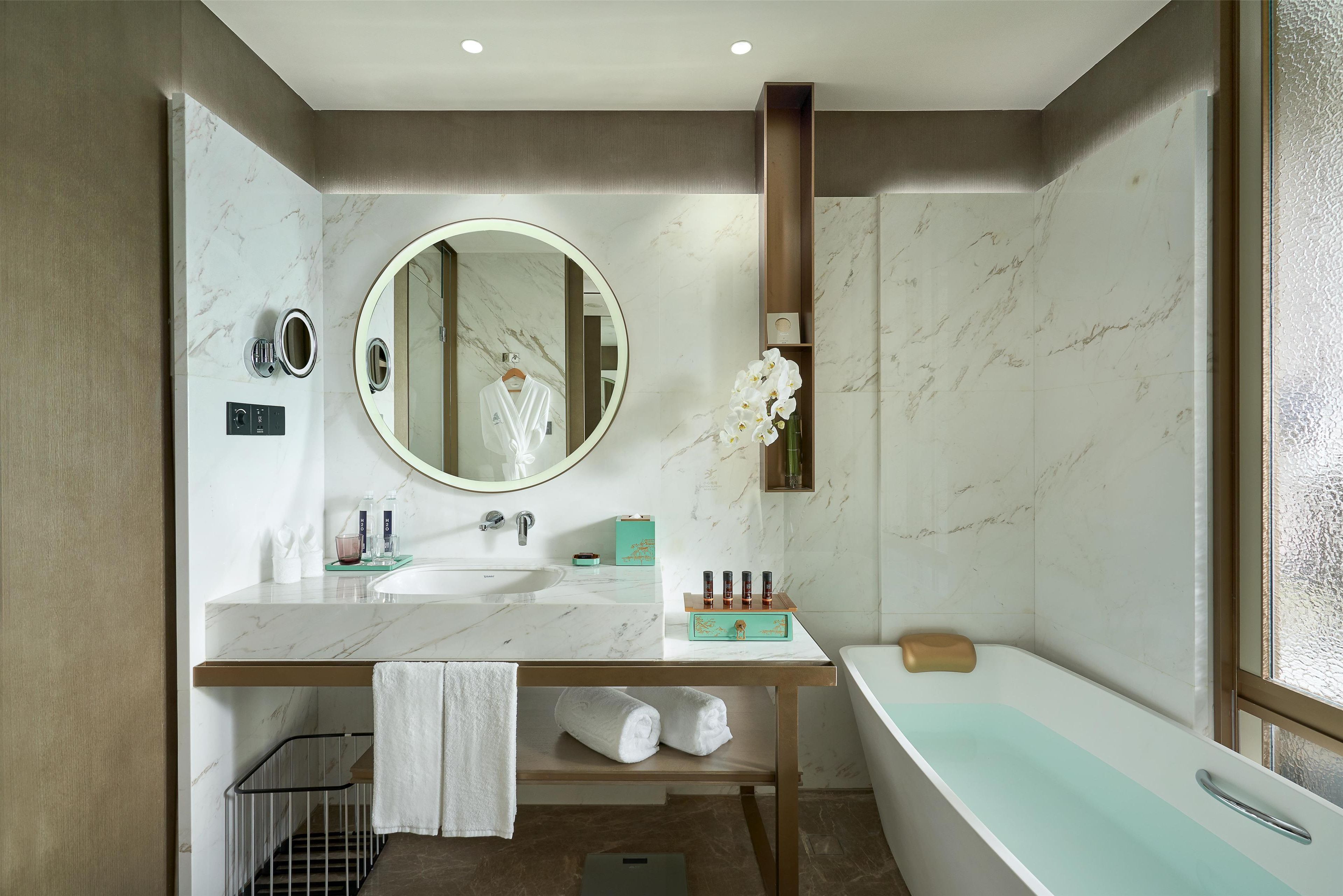 A modern bathroom with a marble sink, a large mirror, a bathtub, and a towel rack.