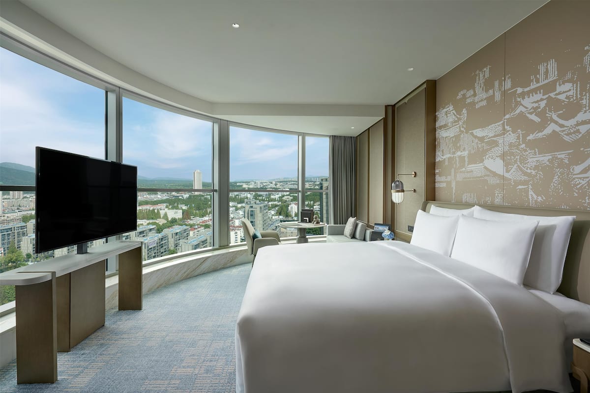 Une chambre d’hôtel dotée d’un grand lit, d’un téléviseur à écran plat, d’un bureau et offrant une vue sur la ville grâce à de grandes fenêtres.