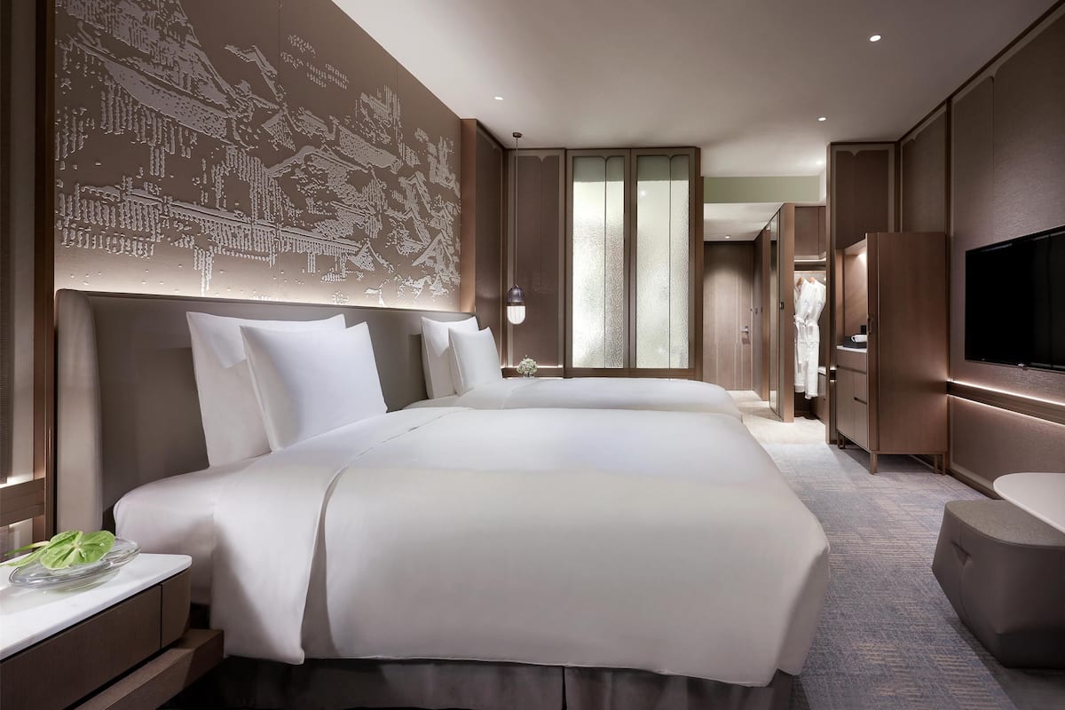 Une chambre d’hôtel spacieuse, dotée d’un grand lit, d’une télévision, d’une armoire et d’un mur décoratif.