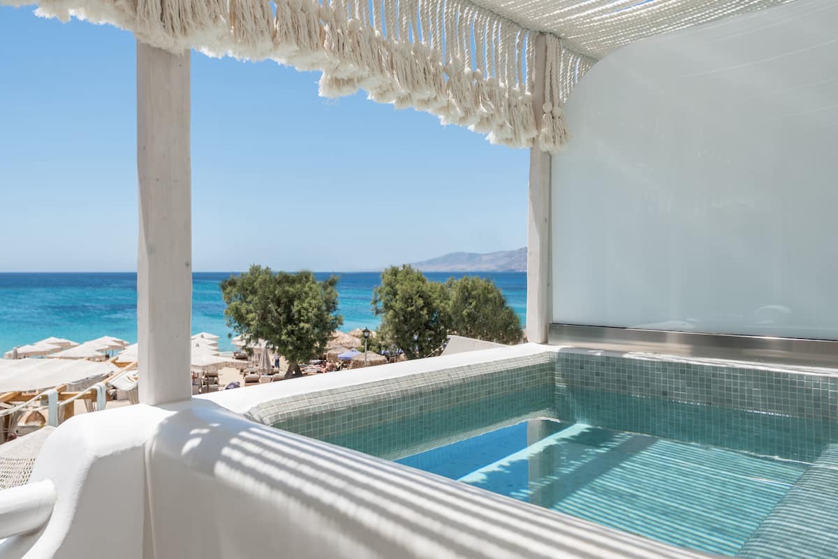 Un espace piscine avec vue sur la mer, des chaises longues blanches et des parasols.