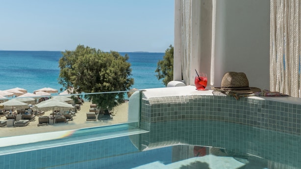 A poolside view with a clear blue sky, a beach, and a tree. - Virtu Suites (Naxos)