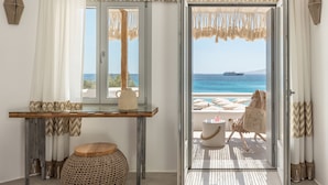 A room with a view of the sea, a table with a vase, a chair, and a woven stool. - Virtu Suites (Naxos)