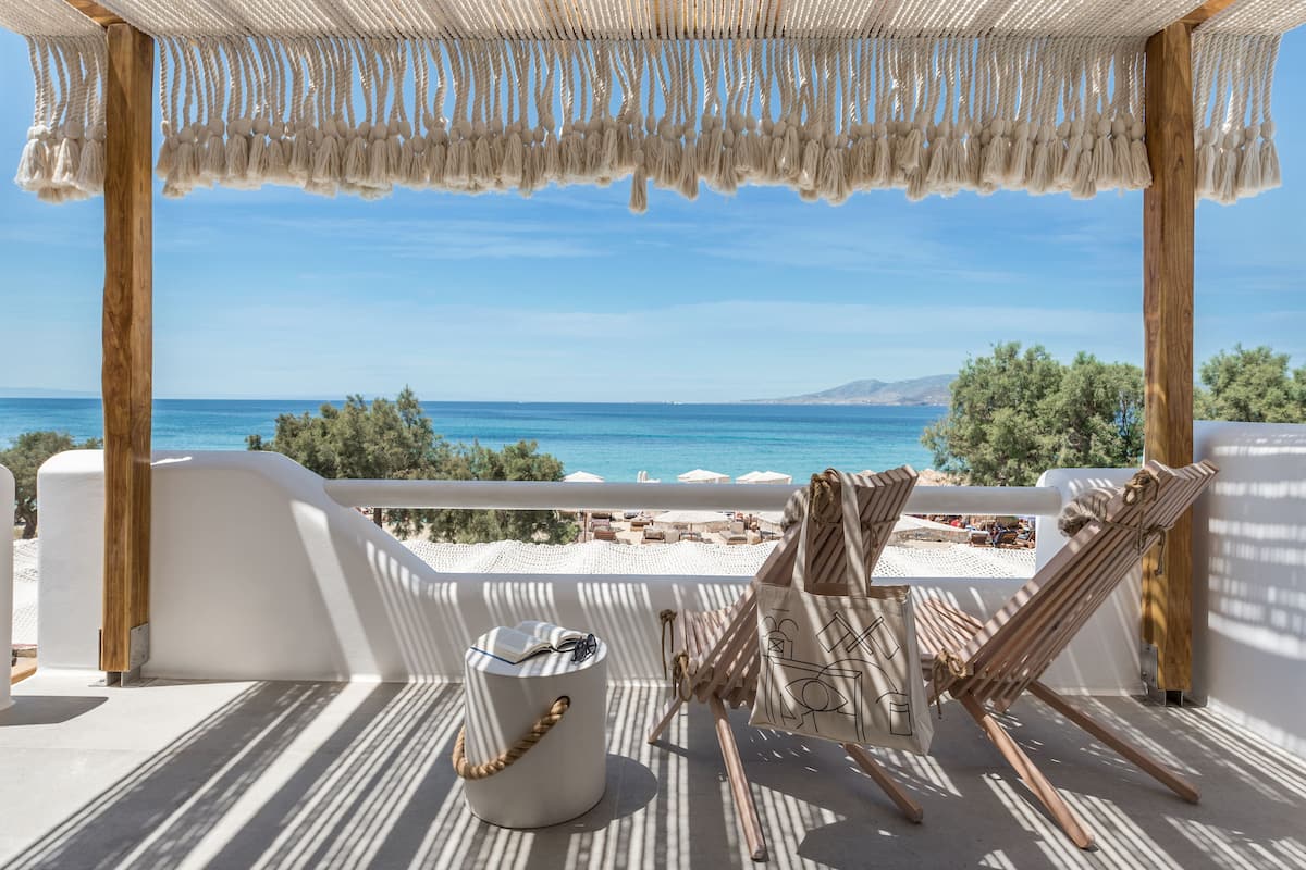 Un balcon avec vue sur la mer, une chaise en bois, un seau blanc et une corde.