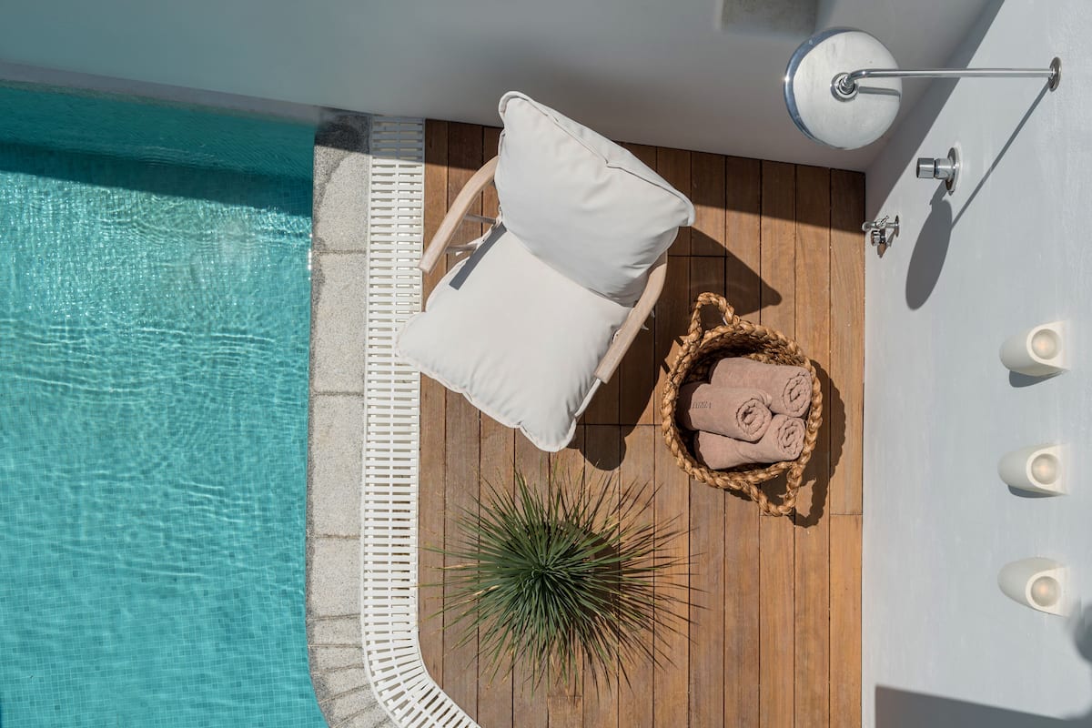 Un espace aménagé au bord de la piscine, avec un fauteuil de relaxation, une petite plante et un panier contenant des serviettes.