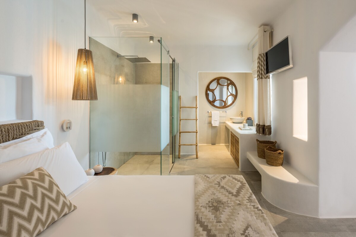 A modern hotel room with a bed, a shower area, a bathroom with a vanity, and a television mounted on the wall.