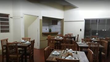 Un comedor con varias mesas y sillas de madera, una zona de cocina con ventana, y una puerta que da a otra habitación.