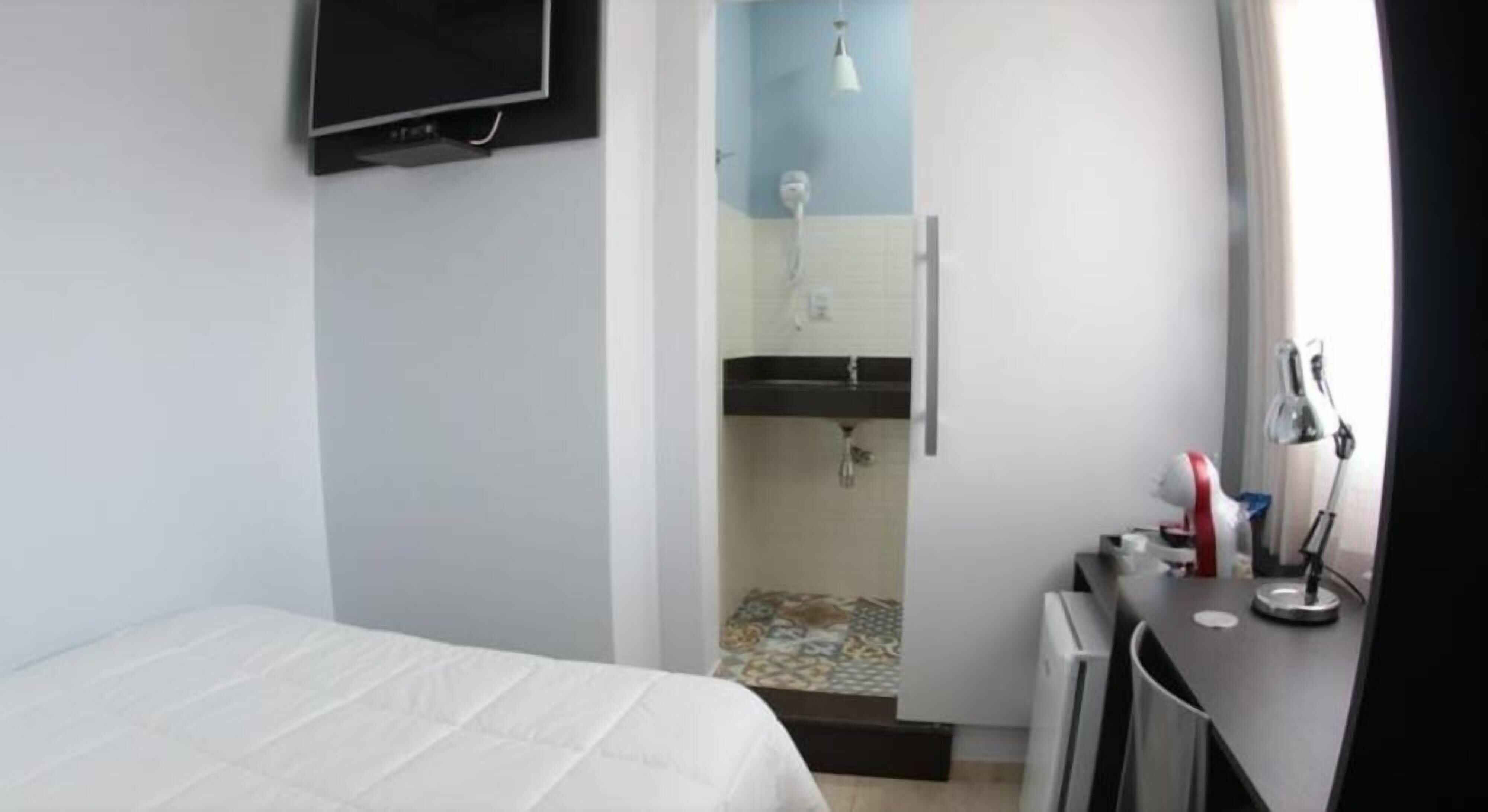 Une chambre d’hôtel équipée d’un lit, d’un téléviseur fixé au mur, d’un espace douche et d’un bureau avec une lampe.