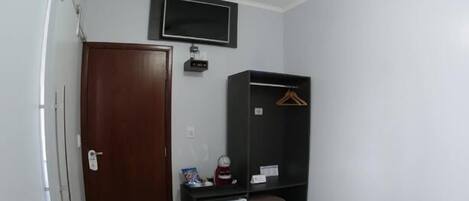 A small, clean room with a bed, a desk with a computer, a TV mounted on the wall, a wardrobe, and a ceiling fan.
