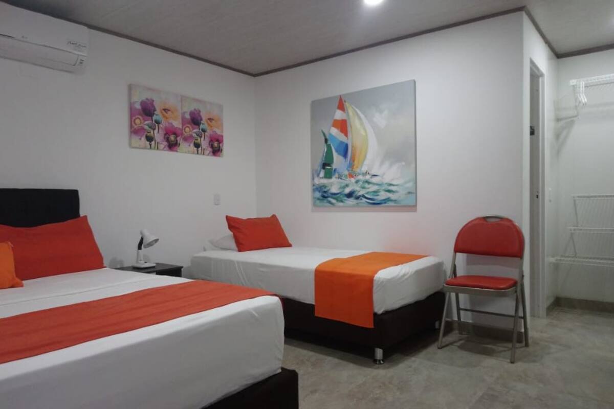 A hotel room with two beds, each with orange bedding, a chair, and a painting of a sailboat on the wall.