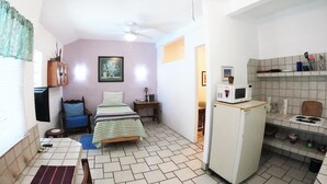 Quarto compacto com cama, pequeno escritório, frigorífico e cozinha americana.