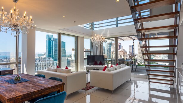 A modern living room with a dining area, large windows, a chandelier, and a city view. - Mirage - WHosting (Cape Town)