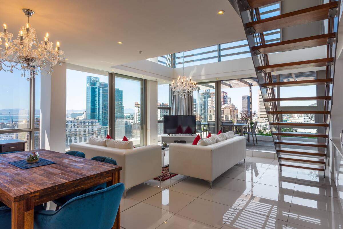A modern living room with a dining area, large windows, a chandelier, and a city view.