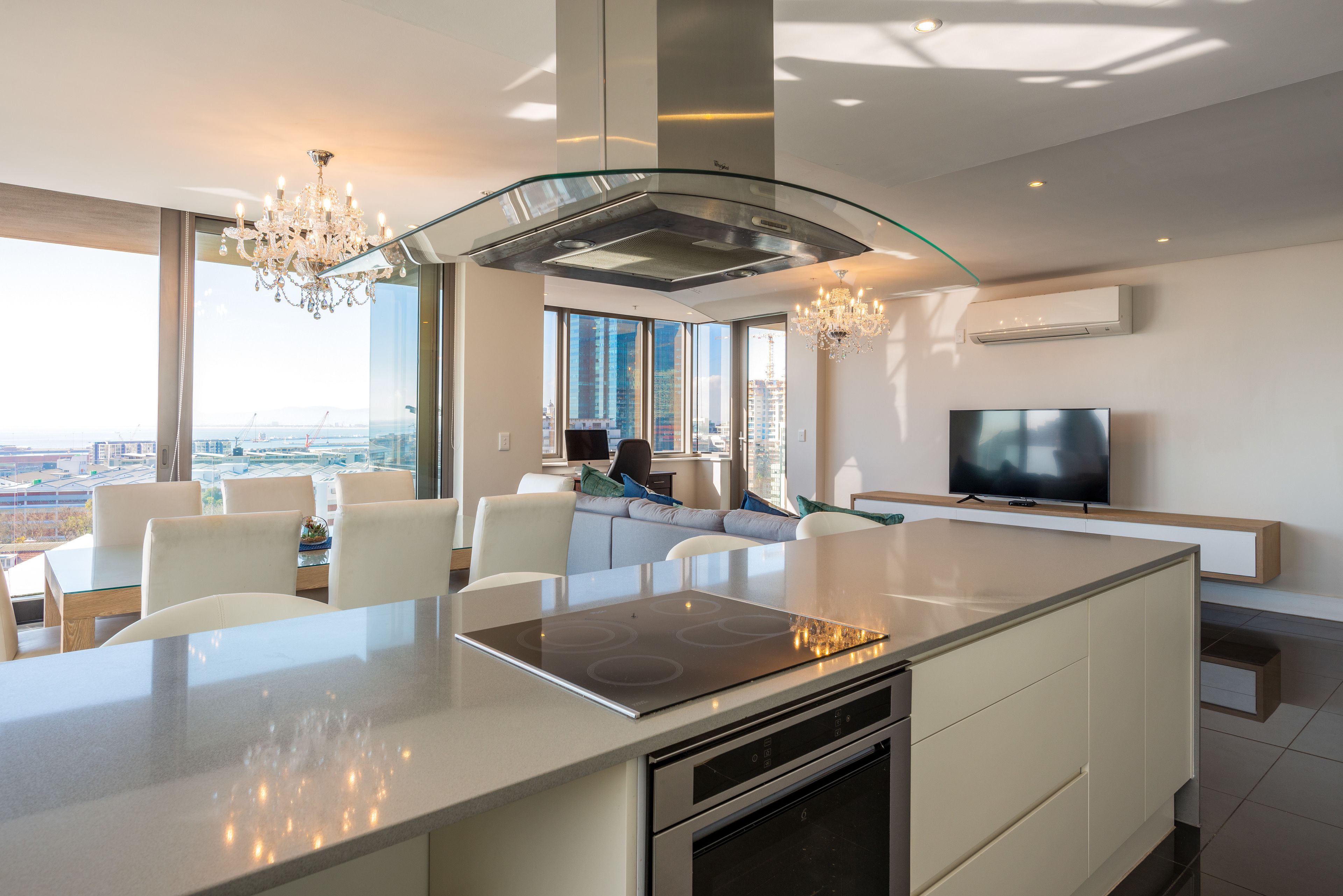 A modern kitchen with a central island, built-in oven, and a large window offering a city view. - Mirage - WHosting (Cape Town)