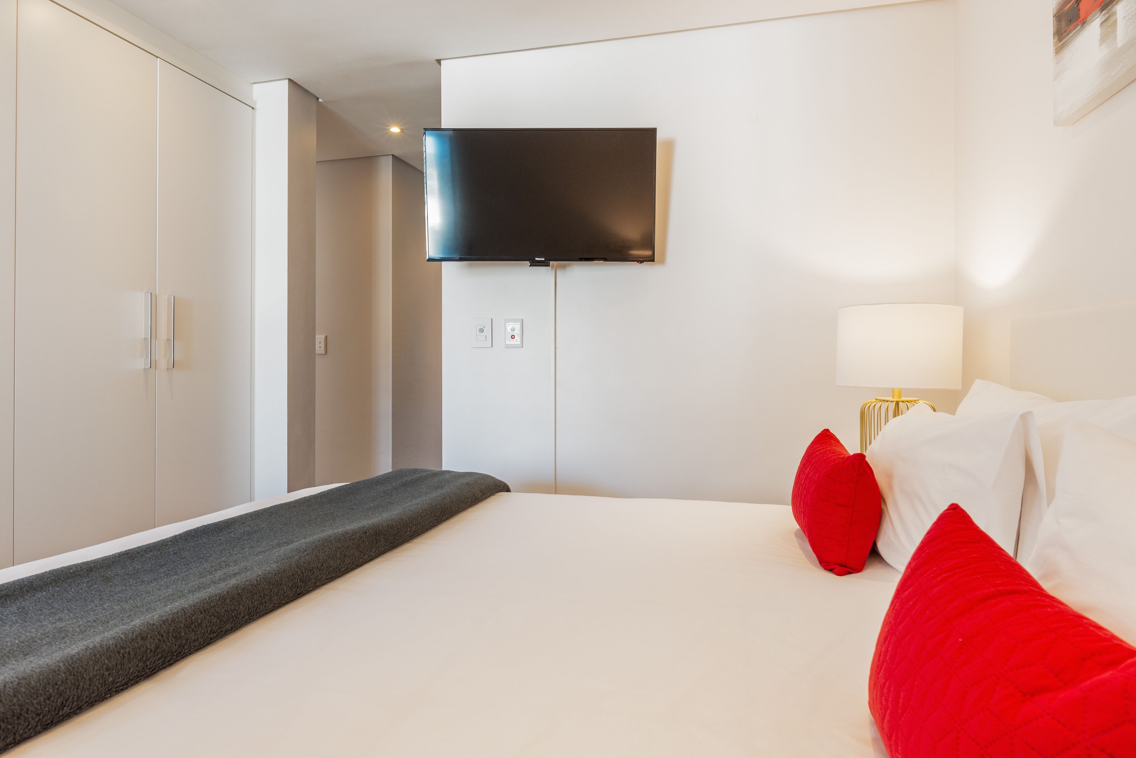 Ein modernes Hotelzimmer mit einem gro ßen Bett, einem flachbildfernseher an der Wand und einem Nachttisch mit einer Lampe.