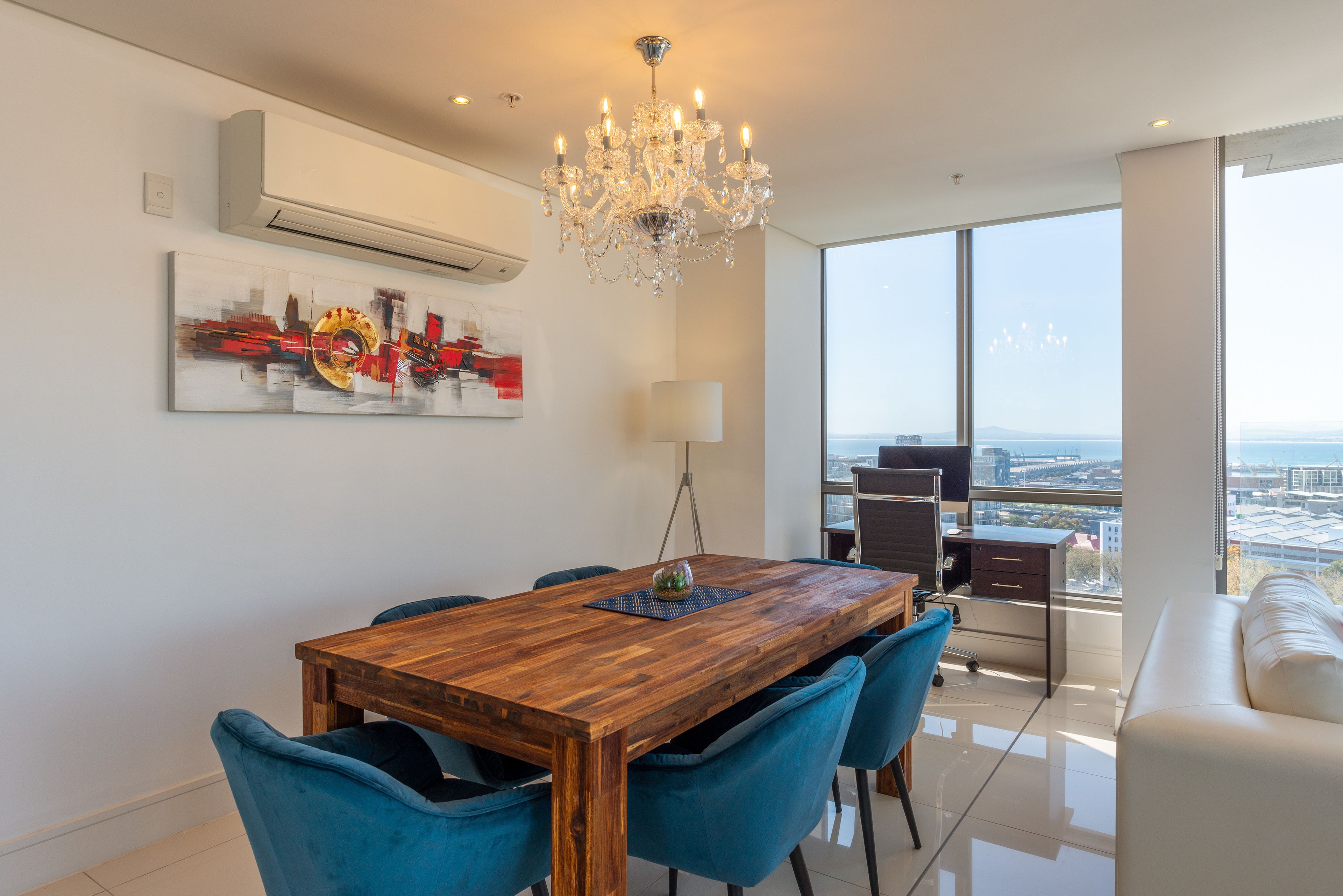 A modern dining area with a wooden table, blue chairs, and a chandelier.