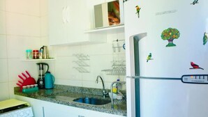 Una cocina con armarios blancos, encimera de granito, estufa, fregadero y refrigerador con imanes.