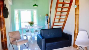 Una sala de estar con un sofá negro, una silla blanca, una escalera de madera y un comedor con una mesa y sillas blancas.