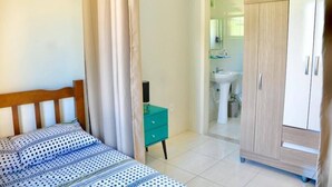 Un dormitorio con cama, mesita de noche, armario y baño visible a través de una puerta abierta.