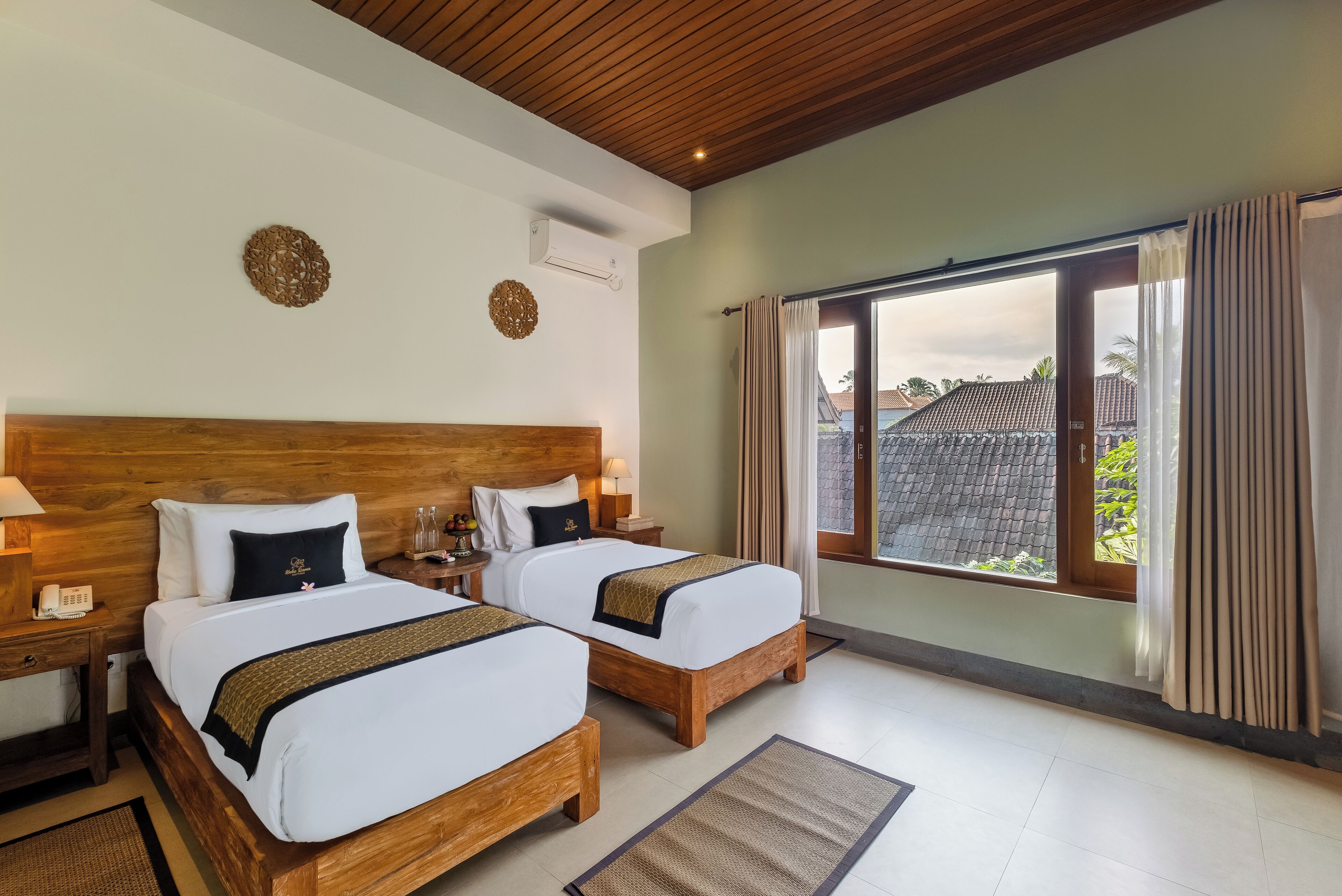 A hotel room with two wooden beds, a large window with curtains, and a view of the outside.