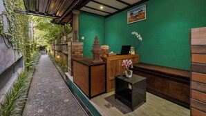 A reception area with a green wall, a wooden reception desk, a small table with a vase, and a bench. - Kubu Rama Ubud Cottage (Ubud)