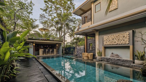 A modern pool area with a clear pool, wooden deck, and tropical plants. - Kubu Rama Ubud Cottage (Ubud)