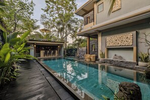 A modern pool area with a clear pool, wooden deck, and tropical plants.
