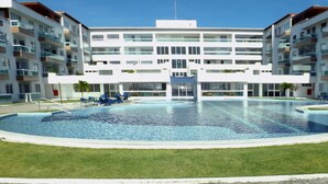 Un bâtiment moderne doté d’une piscine centrale, entouré d’une pelouse bien entretenue et de nombreux balcons.