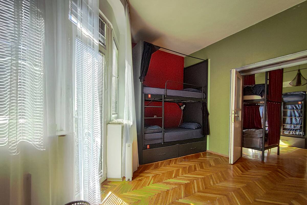 A room with bunk beds, a herringbone-patterned wooden floor, and a window with blinds.