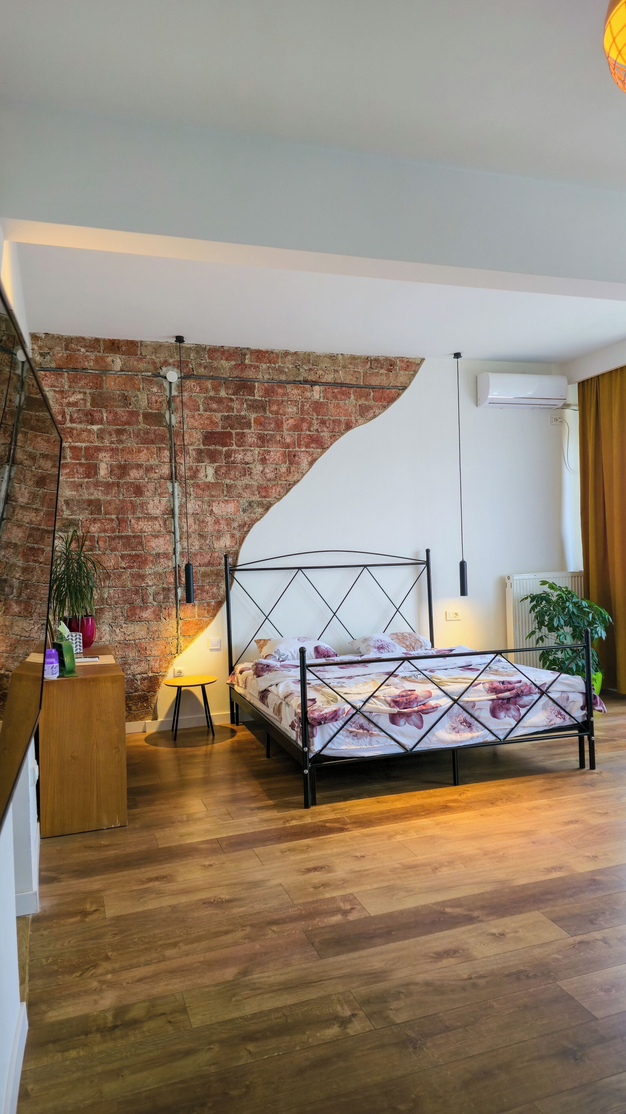 Un dormitorio con pared de ladrillo, una cama con colcha floral, una lámpara de pie y un radiador.