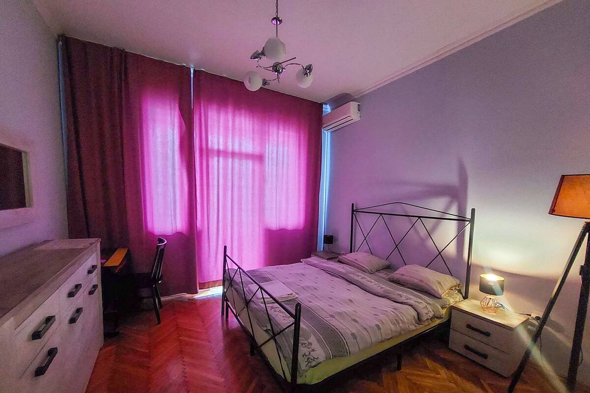 A bedroom with a bed, a dresser, a nightstand, and a lamp.