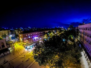 A nighttime cityscape with illuminated buildings, a street with cars, and a tree-lined area. - Prishtina Center Hostel (Pristina)
