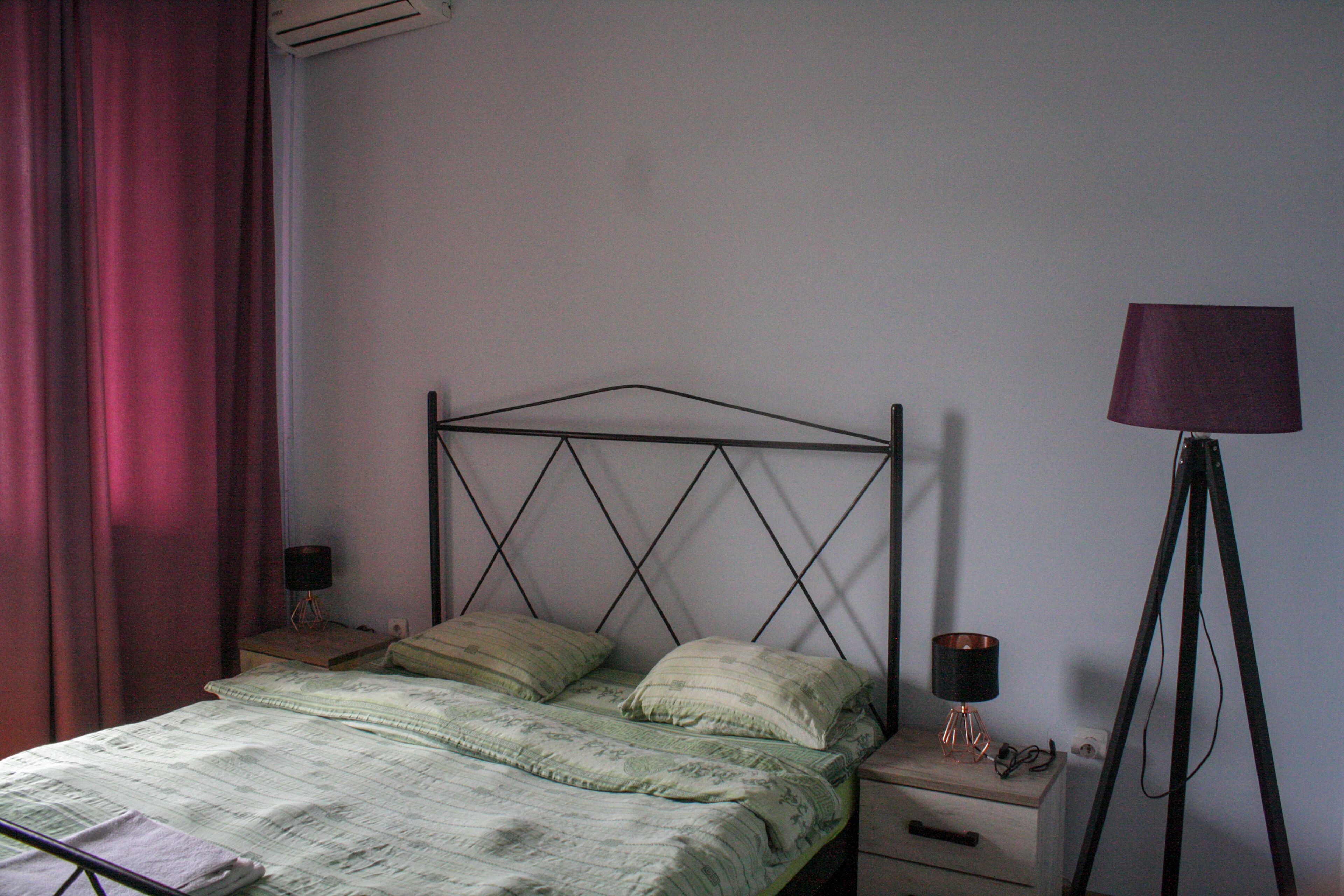 Un dormitorio con cama, mesita de noche, lámpara y ventana con cortinas.