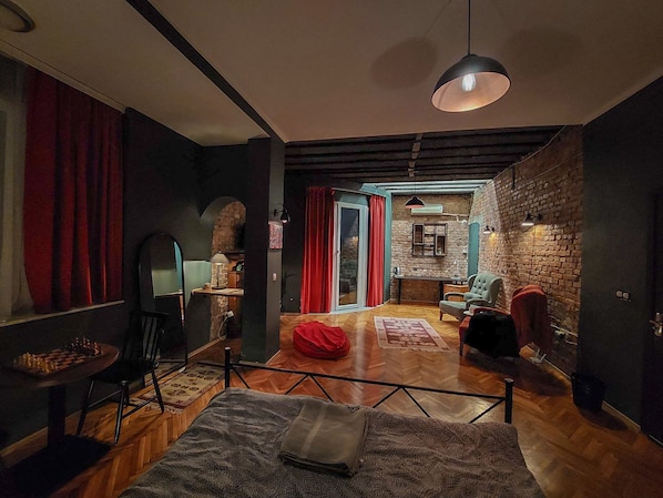 A cozy, well-lit room with a wooden floor, a large bed, a red bean bag, and a dining table with chairs.