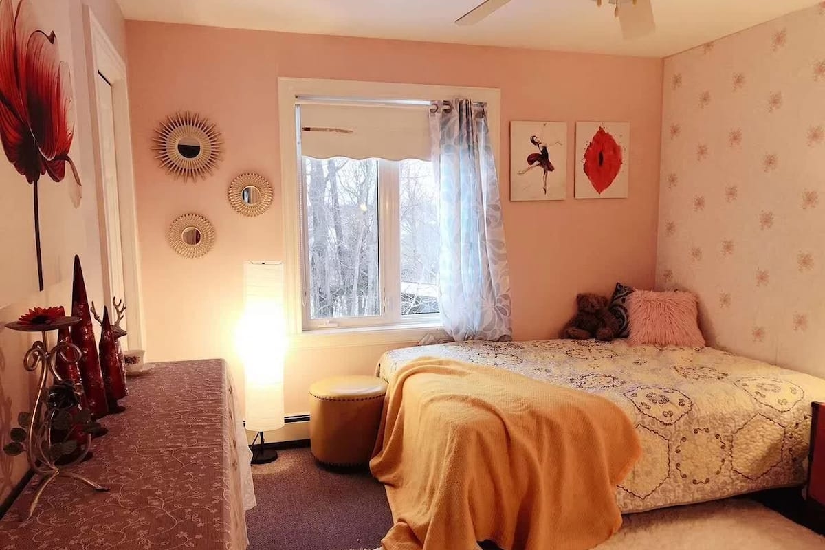 A bedroom with a bed, a window, a bedside table, and a chair.
