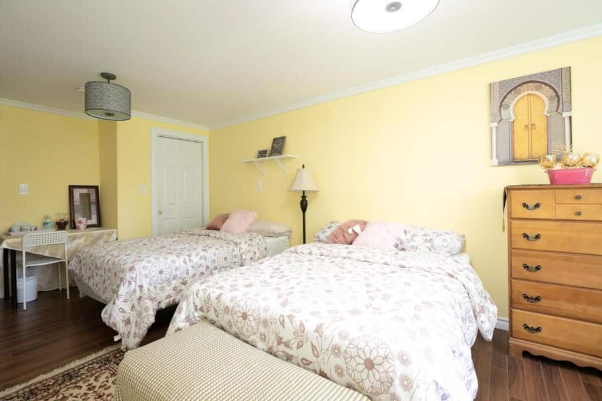 A bedroom with two beds, a desk, a dresser, and a lamp.