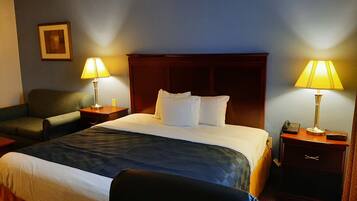 A hotel room with a large bed, two bedside tables, a chair, and a desk with a phone.